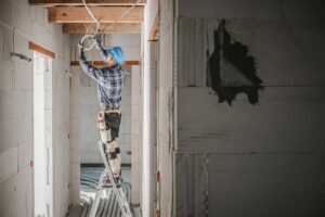 A homeowner examines a tripped breaker beside a residential electrical panel with unplugged appliances nearby.
