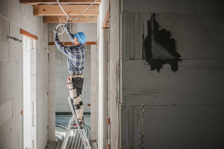 A homeowner examines a tripped breaker beside a residential electrical panel with unplugged appliances nearby.